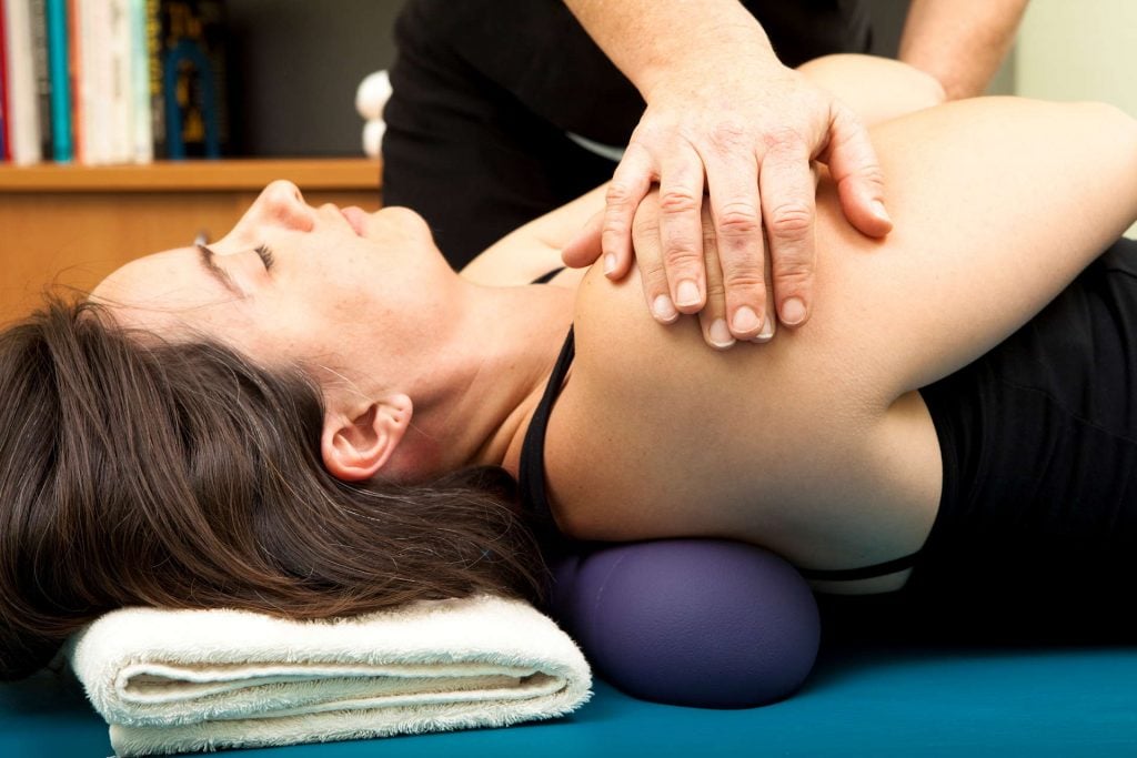 woman receiving physiotherapy on her shoulder with gentle manipulation and her arms crossed lying on her back