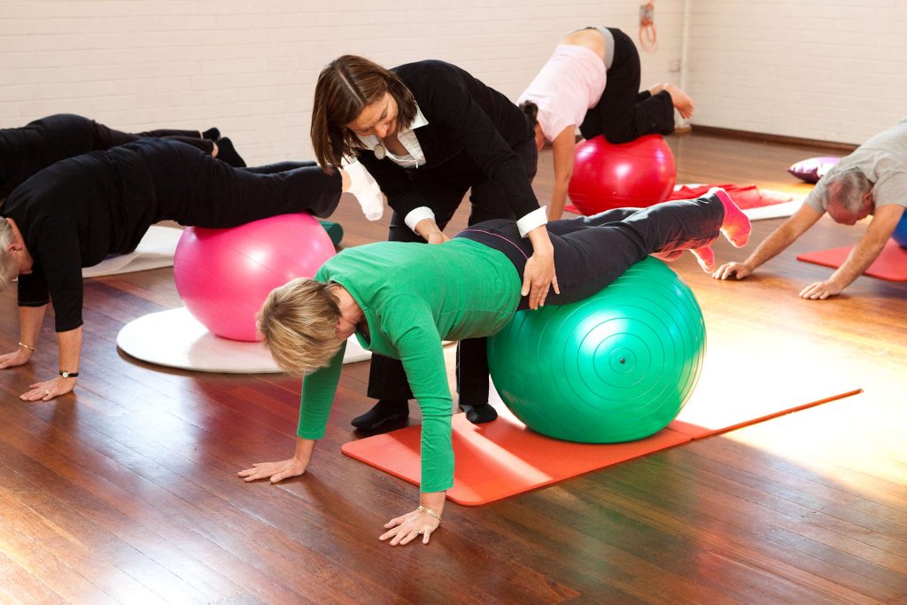 pilates on the ball group class in a hall getting individual assistance from physio Jodie Krantz