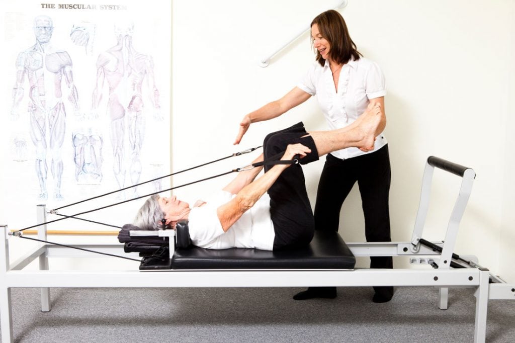 woman on a pilates reformer doing arm raises with legs in table top position being instructed by physiotherapist Jodie Krantz