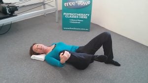 Jodie Krantz on the floor of Free2move Pilates studio on her back holding one knee and the other foot flat on the ground showing a hip freeing exercise.