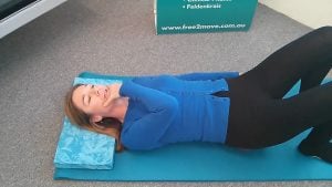 Jodie Krantz lying on the floor in the pilates studio at Free2move holding her jaw.