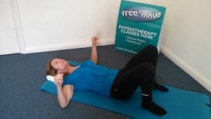 Jodie Krantz on the floor of Free2move pilates studio on her back with her hands lifted showing a way to release shoulder tension.
