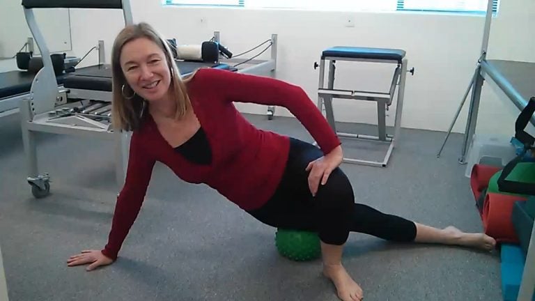 woman massaging itb with mini-ball in a pilates studio