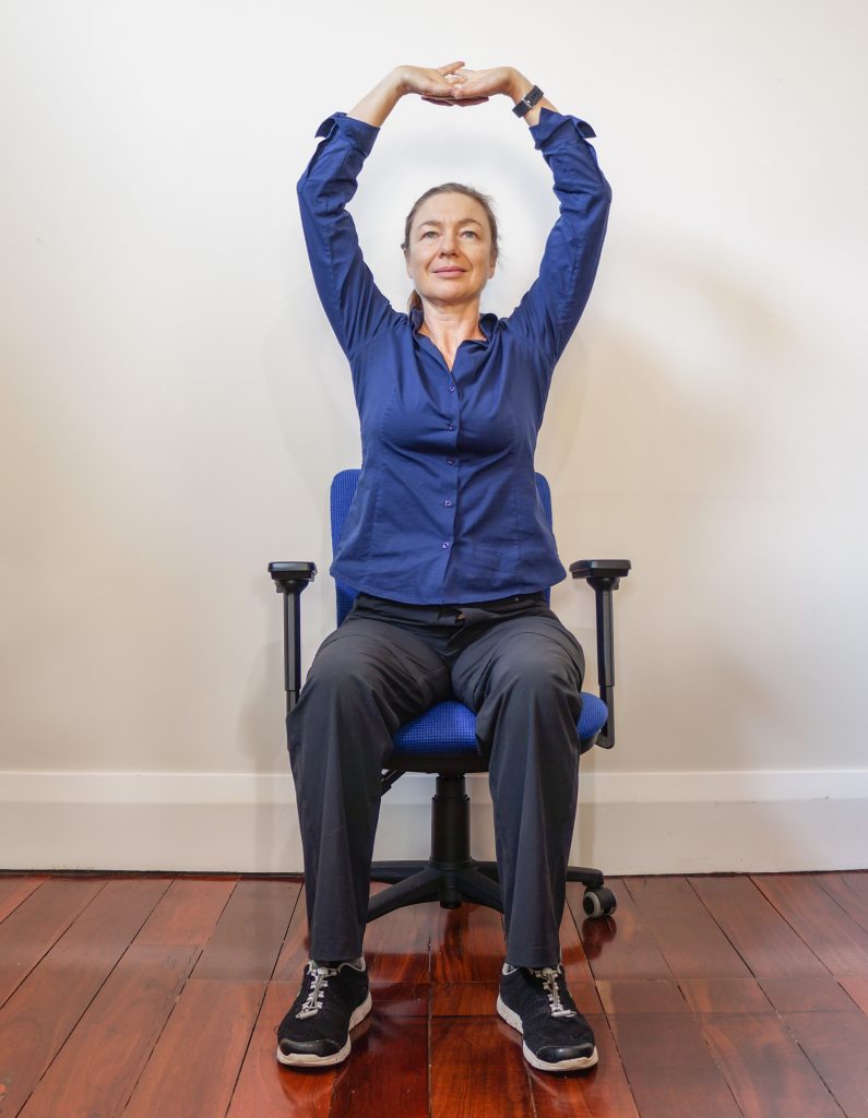 woman sitting on an office chair with her hands interleaved over her head stretching